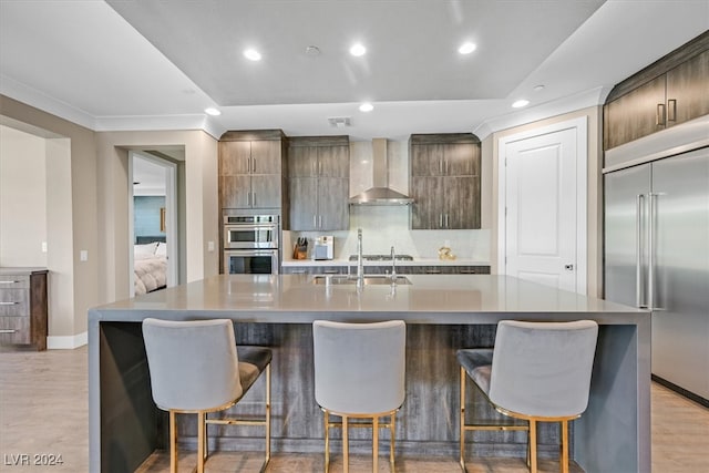 kitchen with an island with sink, stainless steel appliances, and wall chimney range hood