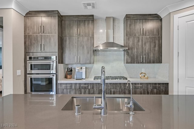 kitchen with appliances with stainless steel finishes, decorative backsplash, sink, and wall chimney range hood