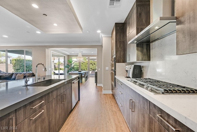 kitchen featuring appliances with stainless steel finishes, light hardwood / wood-style floors, backsplash, wall chimney exhaust hood, and sink