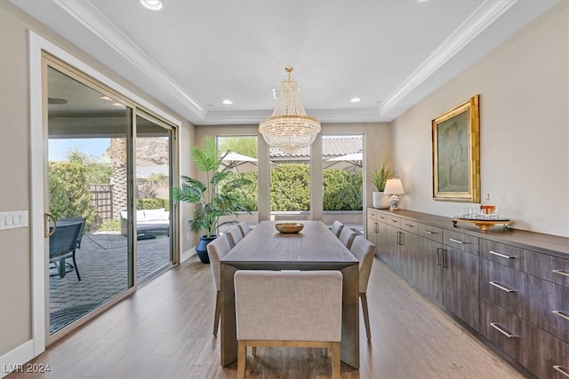 dining area featuring light hardwood / wood-style flooring, a notable chandelier, a raised ceiling, and crown molding