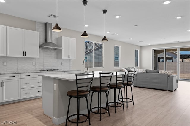 kitchen featuring hanging light fixtures, light stone counters, white cabinets, wall chimney exhaust hood, and light hardwood / wood-style flooring