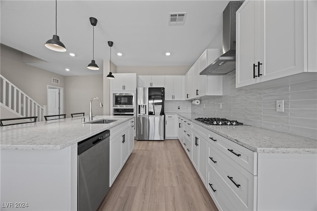 kitchen with white cabinets, wall chimney exhaust hood, pendant lighting, stainless steel appliances, and light wood-type flooring