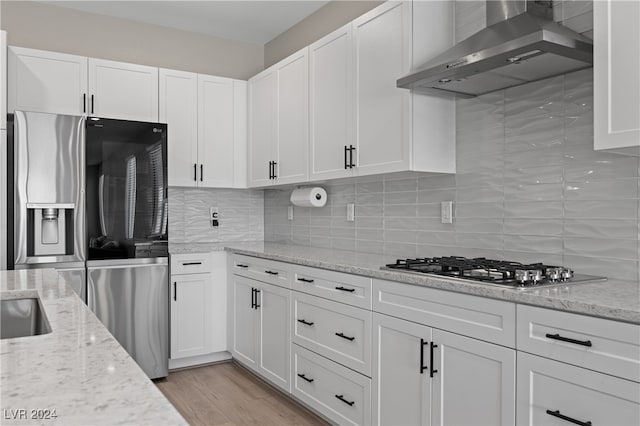 kitchen featuring white cabinets, light stone countertops, stainless steel appliances, light wood-type flooring, and wall chimney range hood