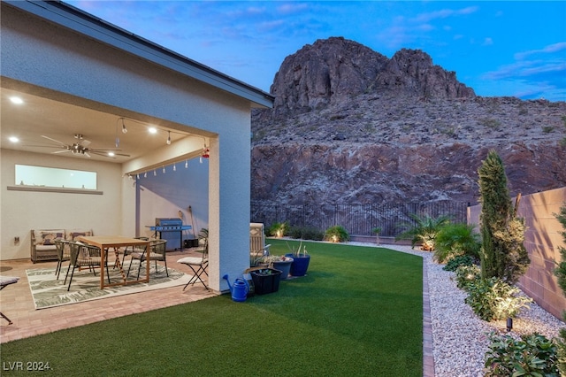 yard at dusk featuring a mountain view, ceiling fan, and a patio area