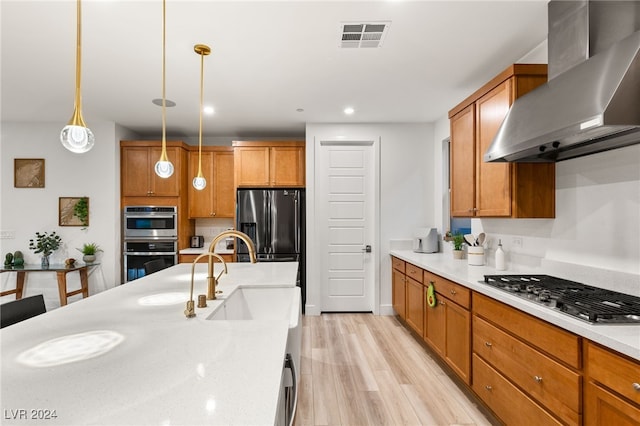 kitchen with hanging light fixtures, sink, wall chimney exhaust hood, appliances with stainless steel finishes, and light wood-type flooring