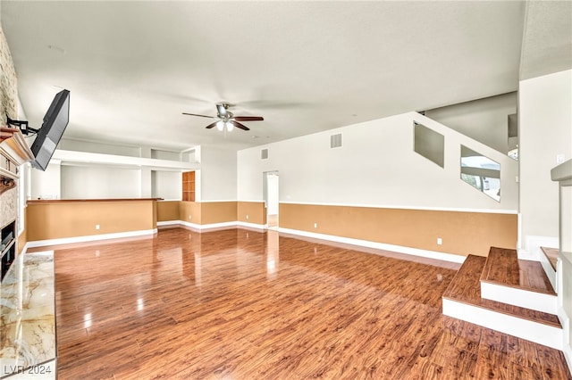 unfurnished living room featuring a stone fireplace, ceiling fan, and hardwood / wood-style flooring