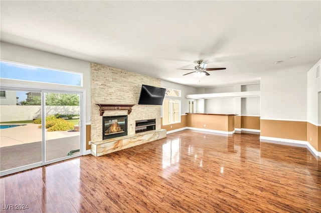 unfurnished living room with ceiling fan, a stone fireplace, hardwood / wood-style floors, and a textured ceiling