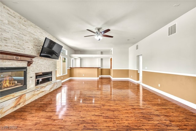 unfurnished living room featuring ceiling fan, a stone fireplace, and hardwood / wood-style floors