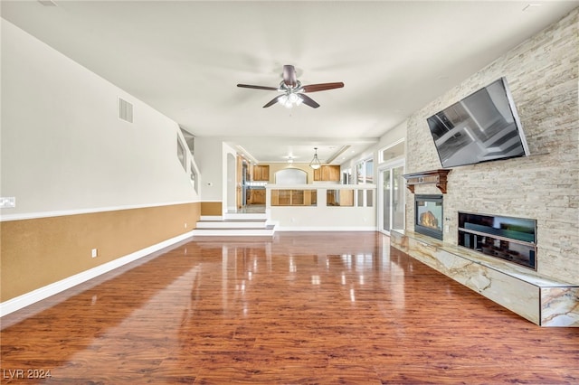 unfurnished living room featuring ceiling fan, wood-type flooring, and a stone fireplace