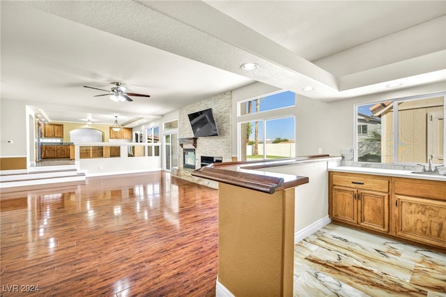 kitchen with a stone fireplace, sink, ceiling fan, kitchen peninsula, and light hardwood / wood-style flooring