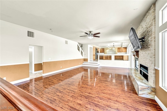 unfurnished living room with a stone fireplace, ceiling fan, and hardwood / wood-style flooring