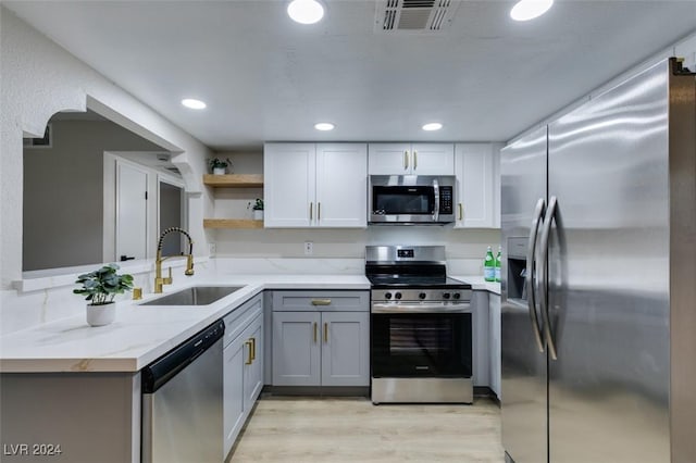 kitchen featuring kitchen peninsula, appliances with stainless steel finishes, light stone counters, gray cabinetry, and sink