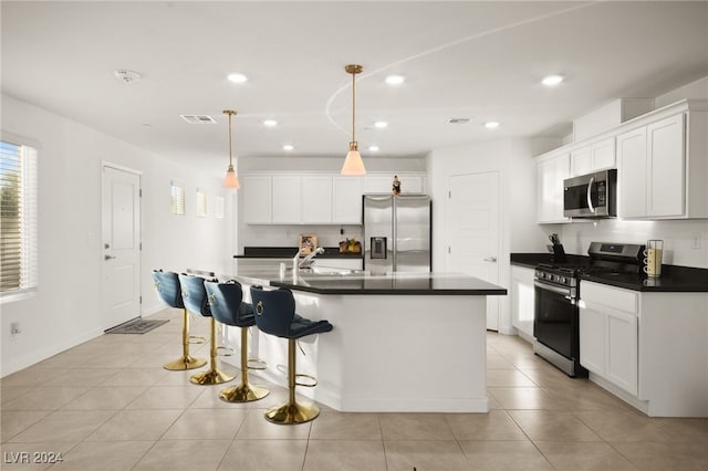 kitchen with an island with sink, light tile patterned flooring, decorative light fixtures, white cabinetry, and stainless steel appliances