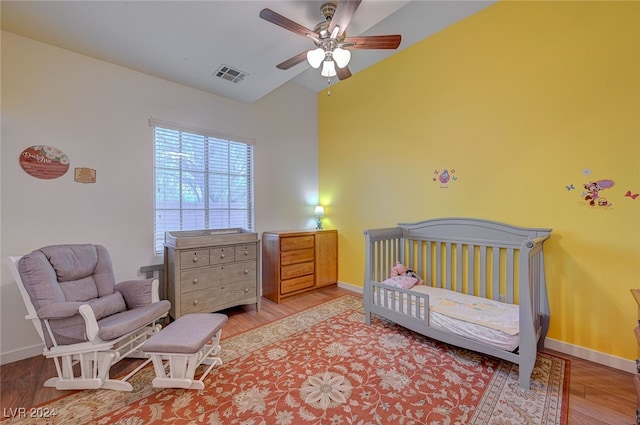 bedroom with light hardwood / wood-style flooring, lofted ceiling, ceiling fan, and a nursery area