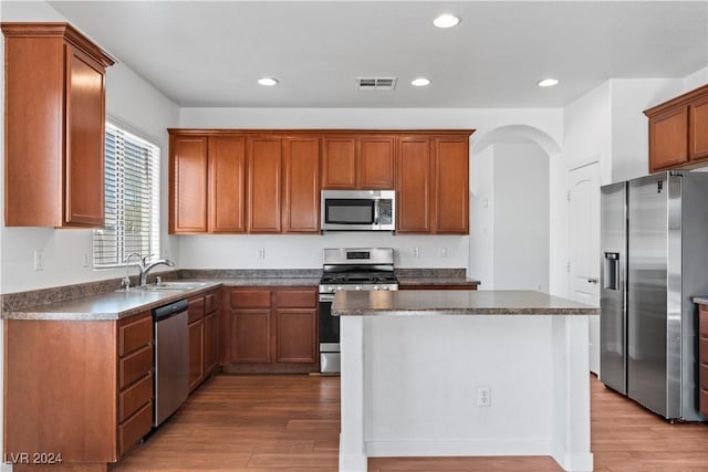 kitchen with appliances with stainless steel finishes, wood-type flooring, sink, and a kitchen island