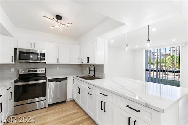 kitchen featuring stainless steel appliances, kitchen peninsula, decorative light fixtures, white cabinets, and light wood-type flooring