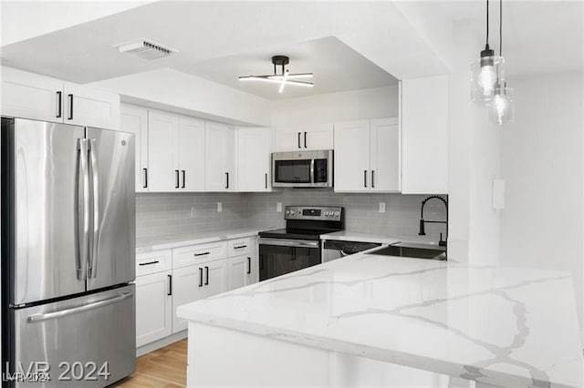 kitchen featuring white cabinetry, sink, light stone counters, appliances with stainless steel finishes, and hanging light fixtures