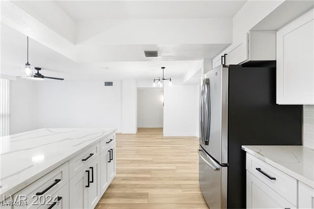 kitchen featuring white cabinets, light stone countertops, pendant lighting, light wood-type flooring, and stainless steel fridge