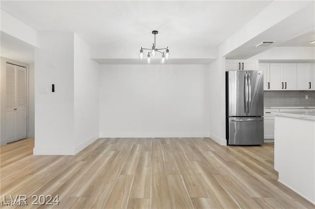 kitchen with stainless steel fridge, white cabinetry, light wood-type flooring, and tasteful backsplash