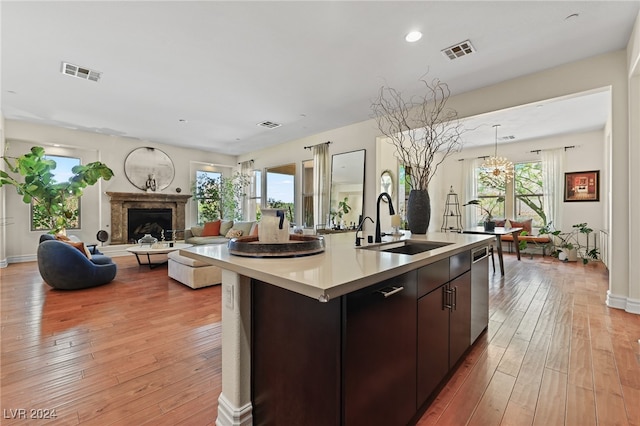 kitchen with dark brown cabinets, dishwasher, a center island with sink, and light hardwood / wood-style flooring