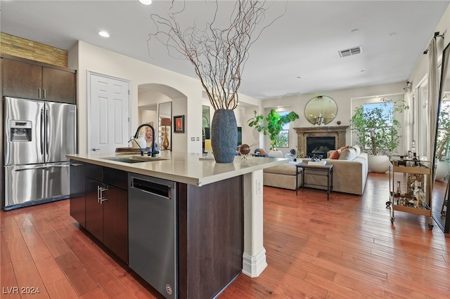 kitchen featuring dark brown cabinets, dark hardwood / wood-style floors, sink, an island with sink, and appliances with stainless steel finishes