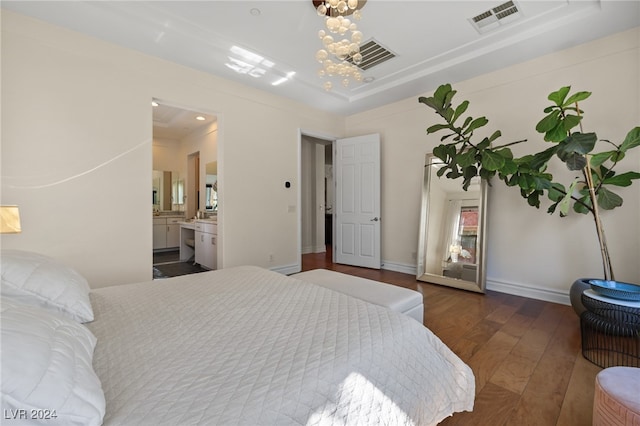 bedroom with connected bathroom, a tray ceiling, dark wood-type flooring, and a chandelier