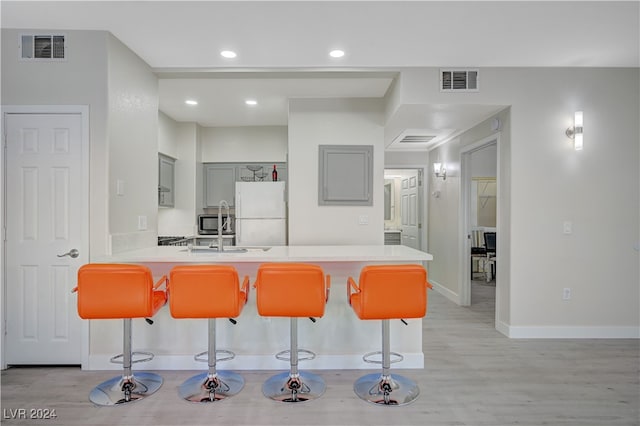 kitchen featuring a kitchen bar, light wood-type flooring, white fridge, and kitchen peninsula