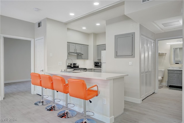 kitchen featuring sink, kitchen peninsula, gray cabinetry, a breakfast bar, and light hardwood / wood-style floors