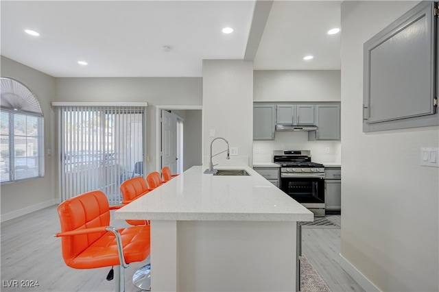 kitchen featuring sink, kitchen peninsula, stainless steel range with gas stovetop, light hardwood / wood-style flooring, and a breakfast bar