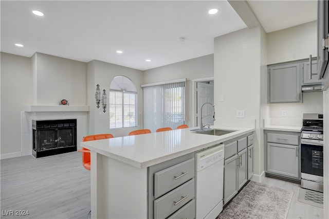 kitchen featuring white dishwasher, sink, kitchen peninsula, stainless steel range, and light hardwood / wood-style floors