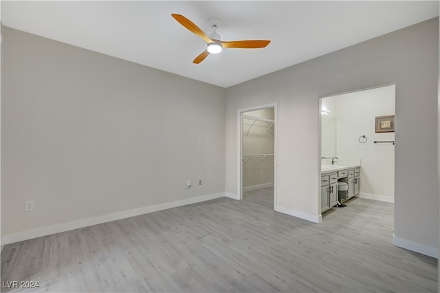 interior space featuring light wood-type flooring, a closet, a walk in closet, ensuite bathroom, and ceiling fan