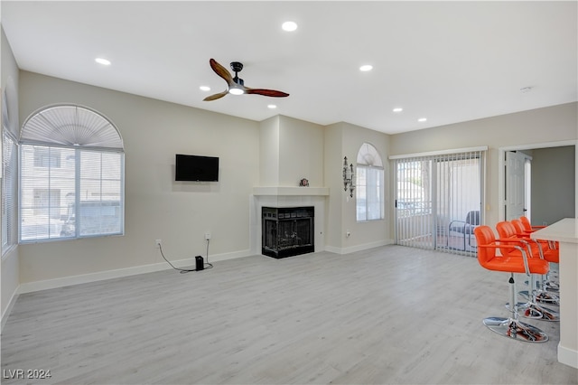 living room featuring light hardwood / wood-style flooring, a wealth of natural light, a multi sided fireplace, and ceiling fan