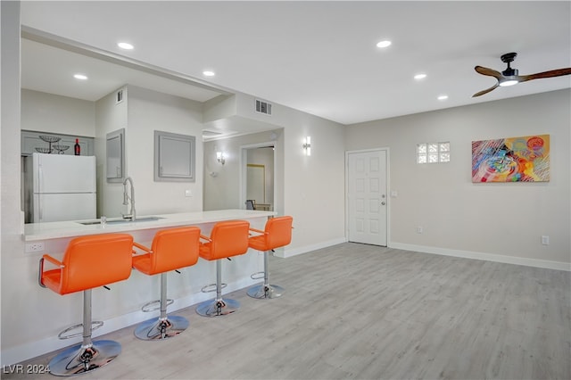 kitchen featuring light wood-type flooring, white refrigerator, a breakfast bar area, kitchen peninsula, and ceiling fan