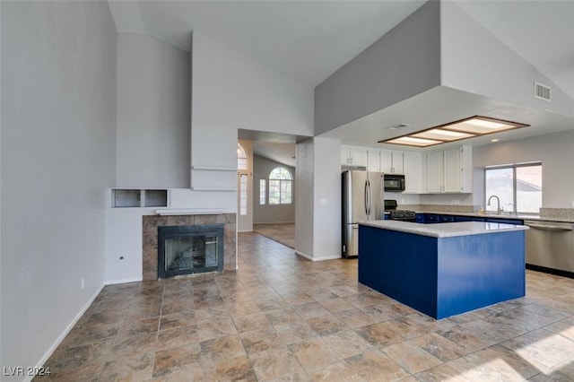 kitchen with white cabinetry, appliances with stainless steel finishes, sink, a tile fireplace, and a center island