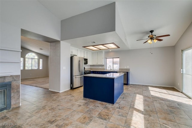 kitchen with stainless steel fridge, lofted ceiling, a fireplace, a kitchen island, and white cabinets