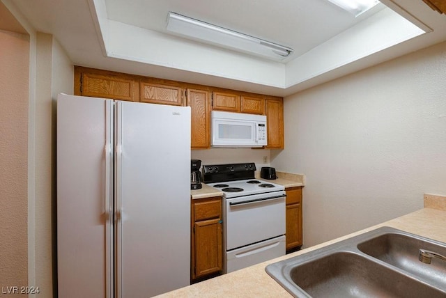 kitchen with brown cabinetry, light countertops, white appliances, and a sink