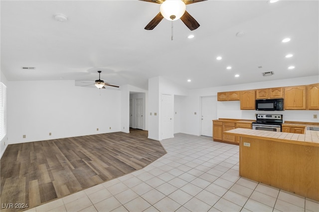 kitchen with light wood-type flooring, vaulted ceiling, ceiling fan, tile counters, and stainless steel range with electric cooktop