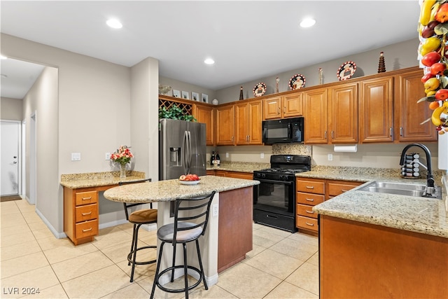 kitchen featuring sink, a kitchen breakfast bar, light stone counters, a kitchen island, and black appliances