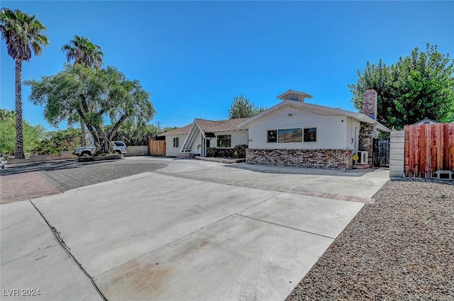 ranch-style home featuring central AC unit, decorative driveway, and fence