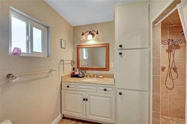 bathroom featuring a tile shower, vanity, and baseboards