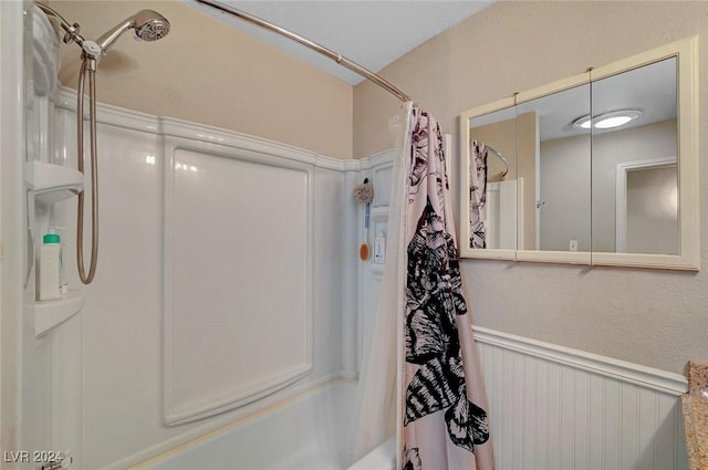 bathroom featuring a wainscoted wall and shower / bath combo