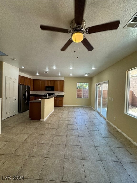 kitchen with stainless steel fridge, light tile patterned floors, a textured ceiling, ceiling fan, and a center island with sink