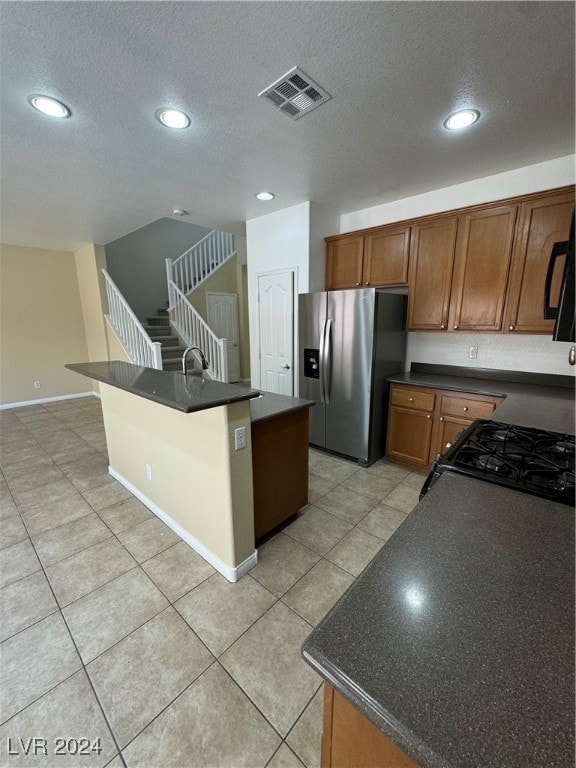 kitchen with a textured ceiling, light tile patterned floors, stainless steel fridge with ice dispenser, and an island with sink