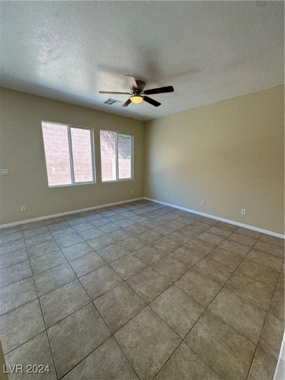 tiled empty room with ceiling fan and a textured ceiling