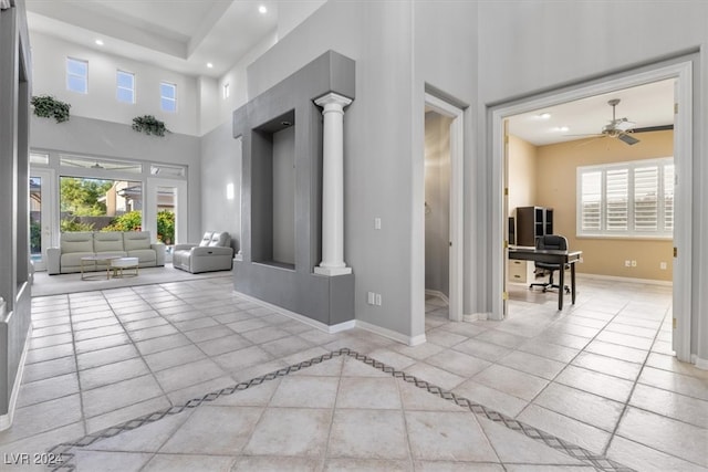 hall featuring a towering ceiling, decorative columns, plenty of natural light, and light tile patterned floors