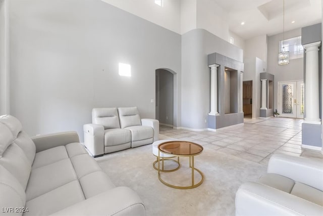 living room with light tile patterned flooring, a towering ceiling, and ornate columns