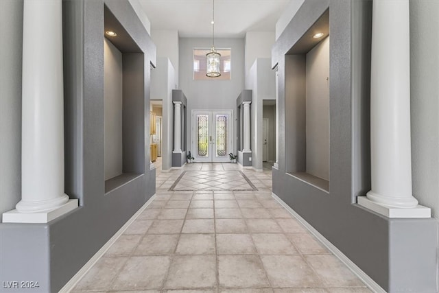 hallway with a towering ceiling, a chandelier, and ornate columns