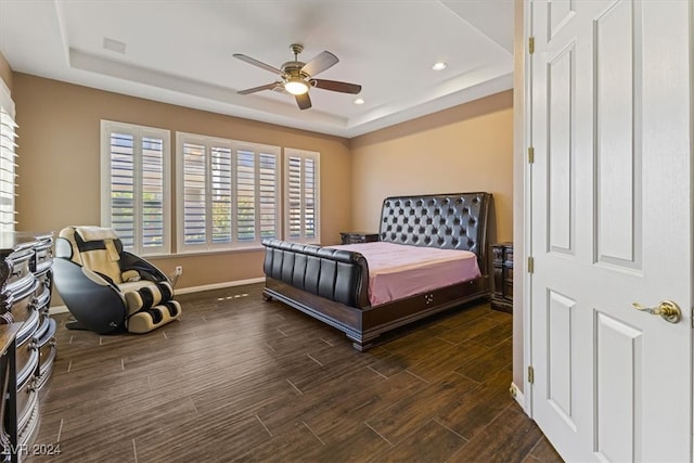 bedroom with ceiling fan, a tray ceiling, and dark wood-type flooring