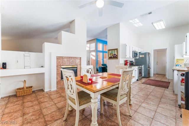 dining area with ceiling fan, a textured ceiling, a tiled fireplace, and high vaulted ceiling