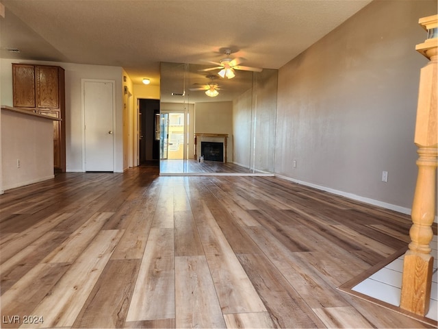 unfurnished living room with light wood-type flooring, a textured ceiling, and ceiling fan